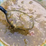 A spoonful of tomatillo salsa held over a bowl of the salsa.