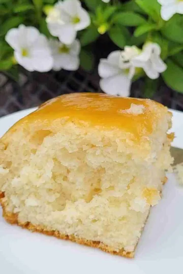 A piece of white cake on a plate in front of white flowers.