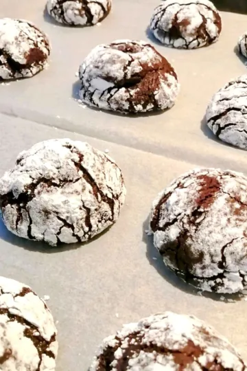 Chocolate crackle cookies on a parchment lined cookie sheet.