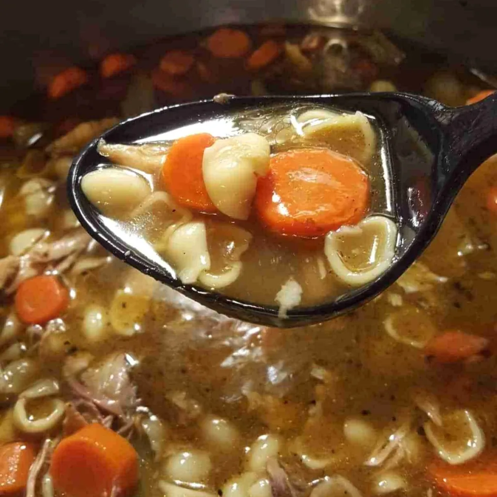 A ladle filled with homemade turkey soup held over a pot of soup.
