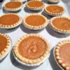 Nine mini pumpkin pies lied up in three rows of three on parchment paper lined tray.