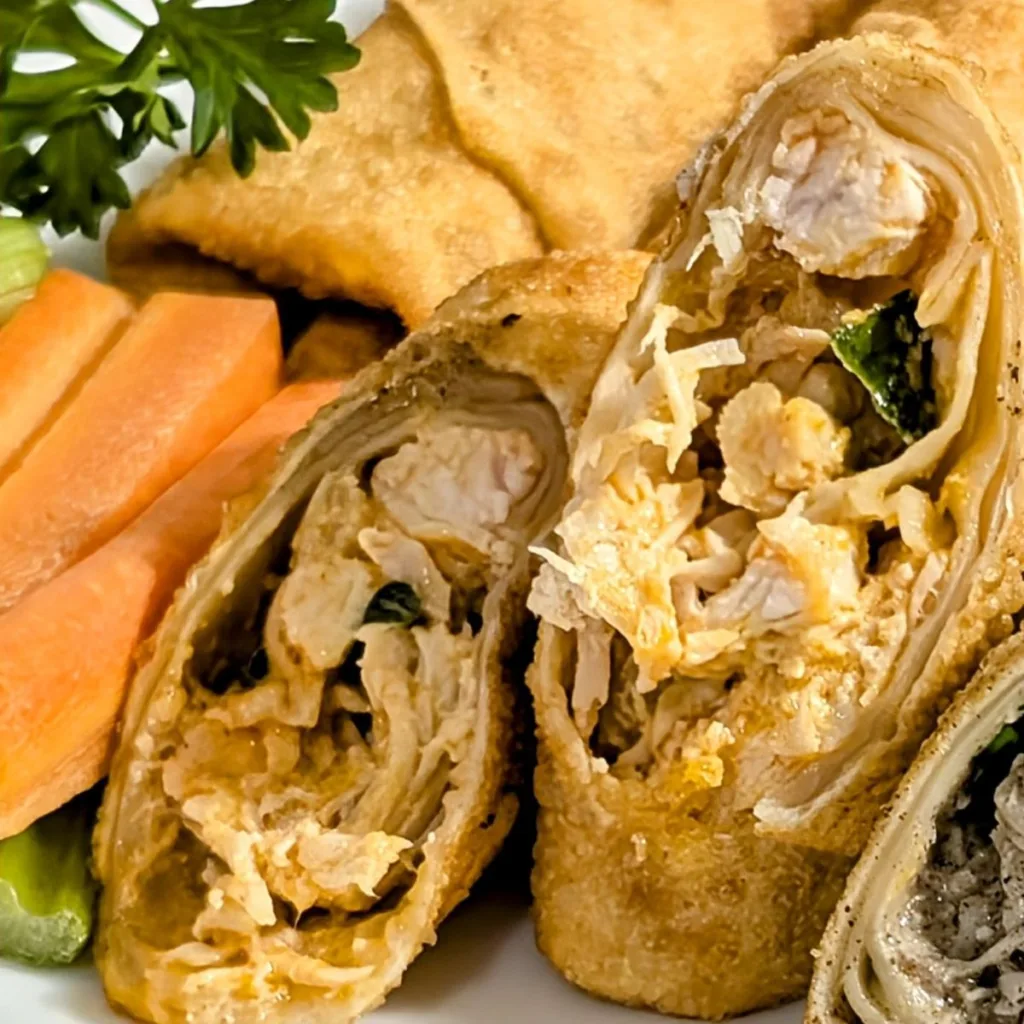 Buffalo Chicken Egg Rolls cut in half on a plate with carrot sticks beside it.