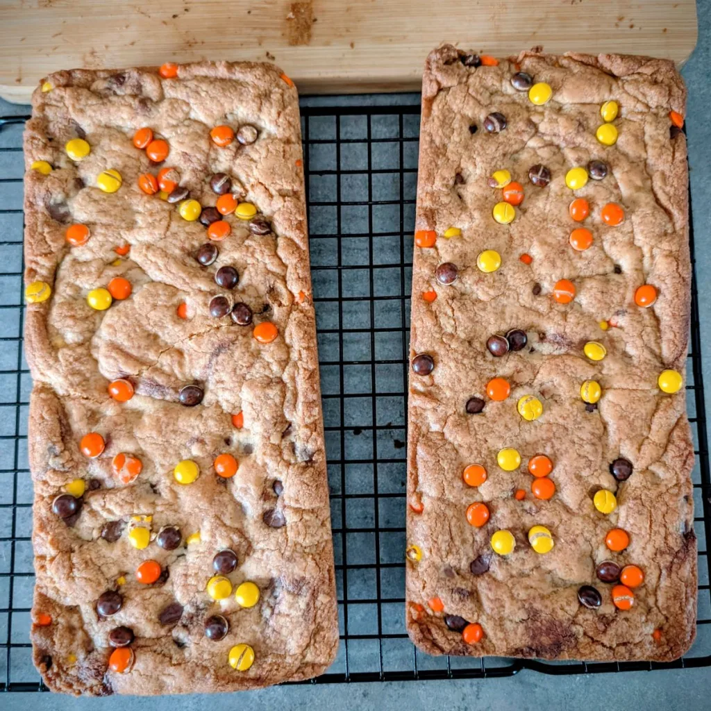 Two Reese's Pieces Cookie Bars on a wire rack.