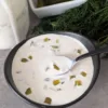 A bowl of Dill Pickle Sauce with a spoon. There is fresh dill and a jar of sauce in the back of the bowl.