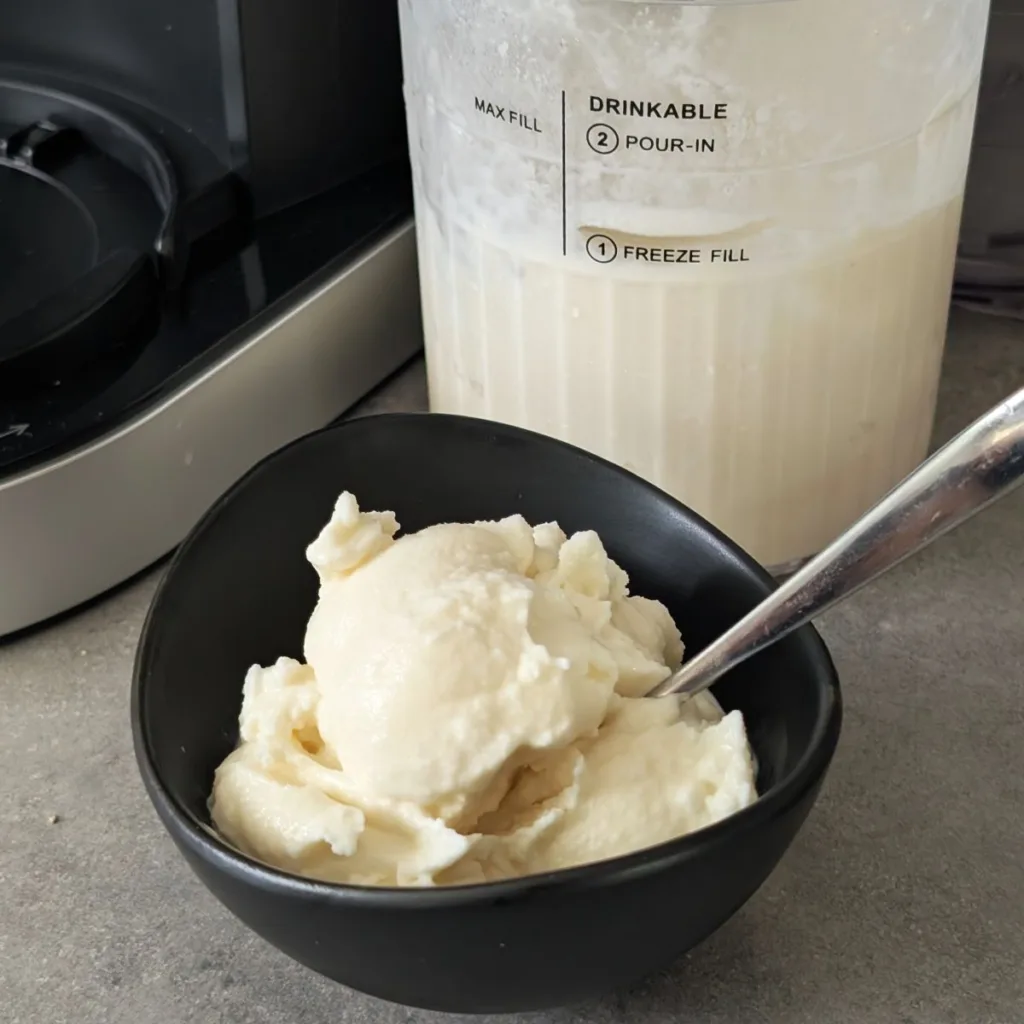 A bowl of Homemade Ice Cream with a spoon. There is a container of ice cream behind it.