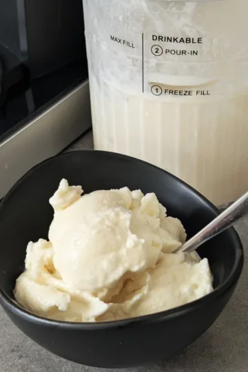 A bowl of Homemade Ice Cream with a spoon. There is a container of ice cream behind it.