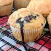 Blueberry Peach Muffin on a cooling rack with more Blueberry Peach Muffins behind the muffin.