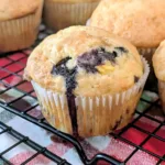 Blueberry Peach Muffin on a cooling rack with more Blueberry Peach Muffins behind the muffin.