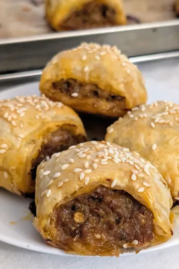 Four Italian Sausage Rolls on a plate with a pan of rolls in the background.