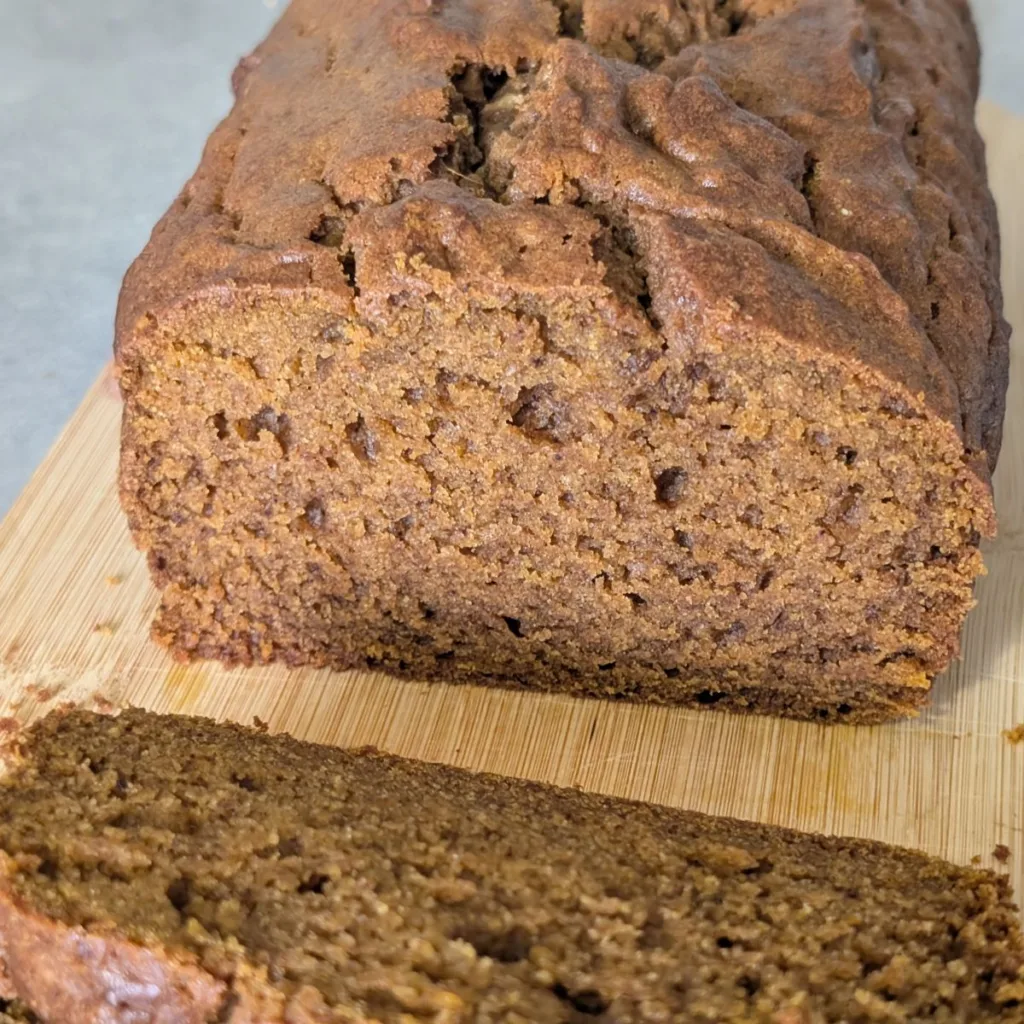 A loaf of pumpkin spice bread sliced open on a cutting board.