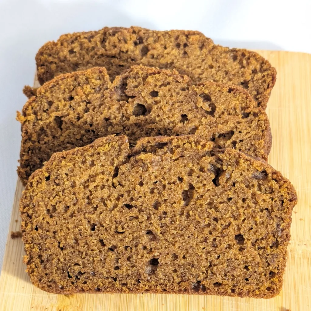 Three slices of pumpkin spice bread fanned on a wooden board.